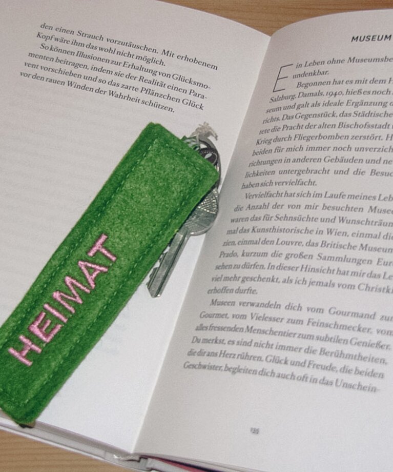 Ein aufgeschlagenes Buch mit einem Zimmerschlüssel darin liegend welcher die Aufschrift "Heimat" hat | © Haus Tannenblick