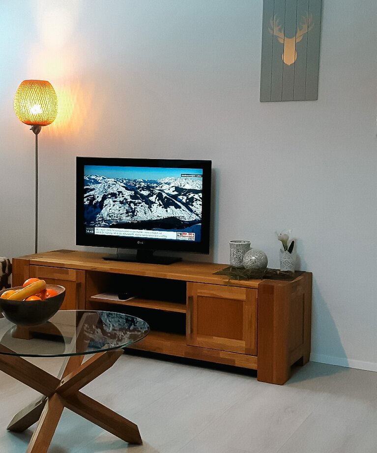 Eine Aufnahme des Wohnbereichs von Appartement 4 - "Schattberg" mit Sofa, Flat-TV und Blick auf den Esstisch in der Küche | © Haus Tannenblick